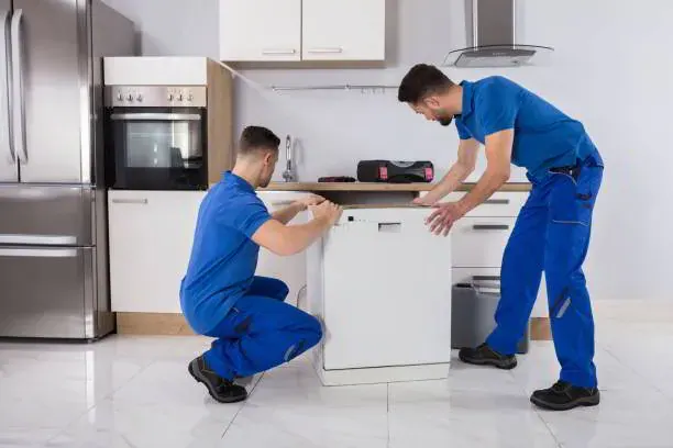 Plumber completing dishwasher installation services under a kitchen counter