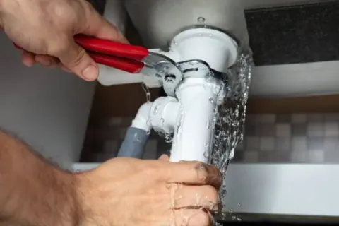 Water spraying from a leaking drain pipe being repaired with pliers
