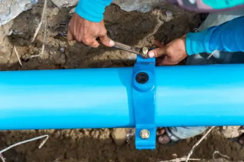 Plumber clamping an exposed underground pipe in an excavation