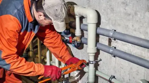 Plumber cutting into a run of gray pipes during a repair