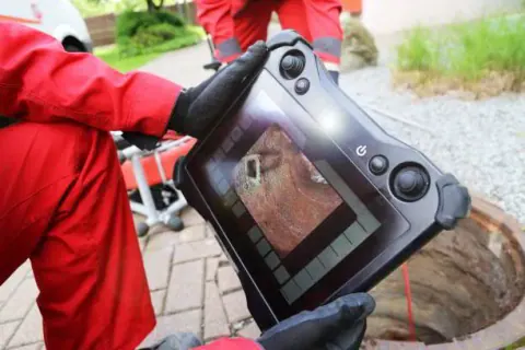 Technician viewing a sewer camera monitor at a cleanout