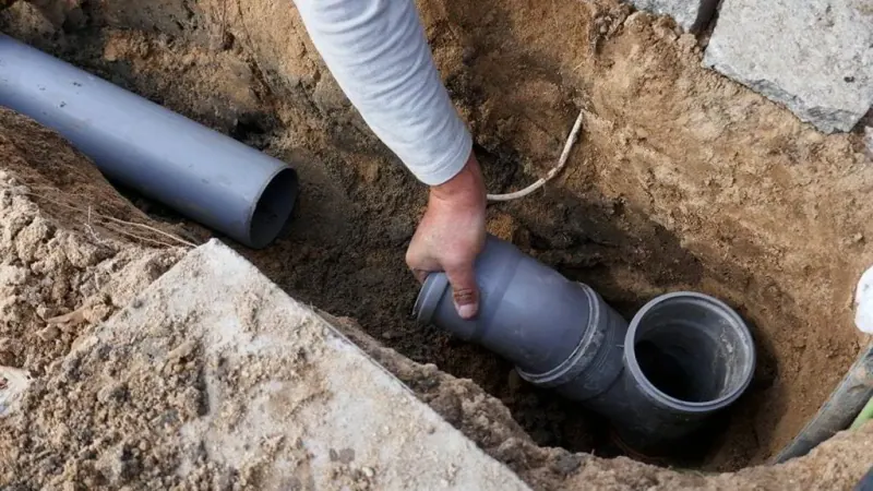Crew performing trenchless pipe repair services through a sewer cleanout beside a paver driveway